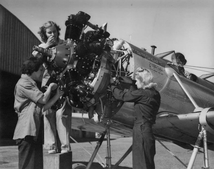 Three women gathered together, working on the front of a small airplane.