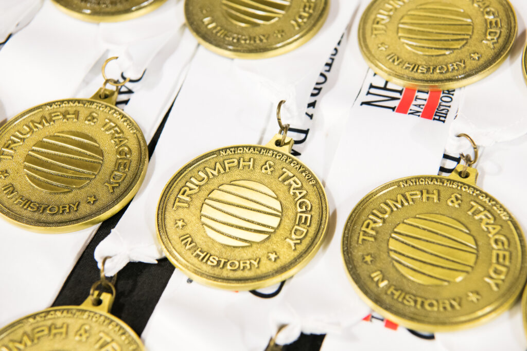 Gold NHD medals with white ribbons laying on a table.