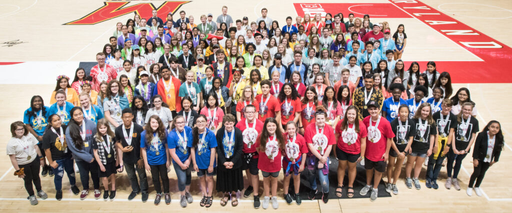 A large group of students standing together in the University of Maryland Xfinity Center wearing NHD medals smiling at the camera.